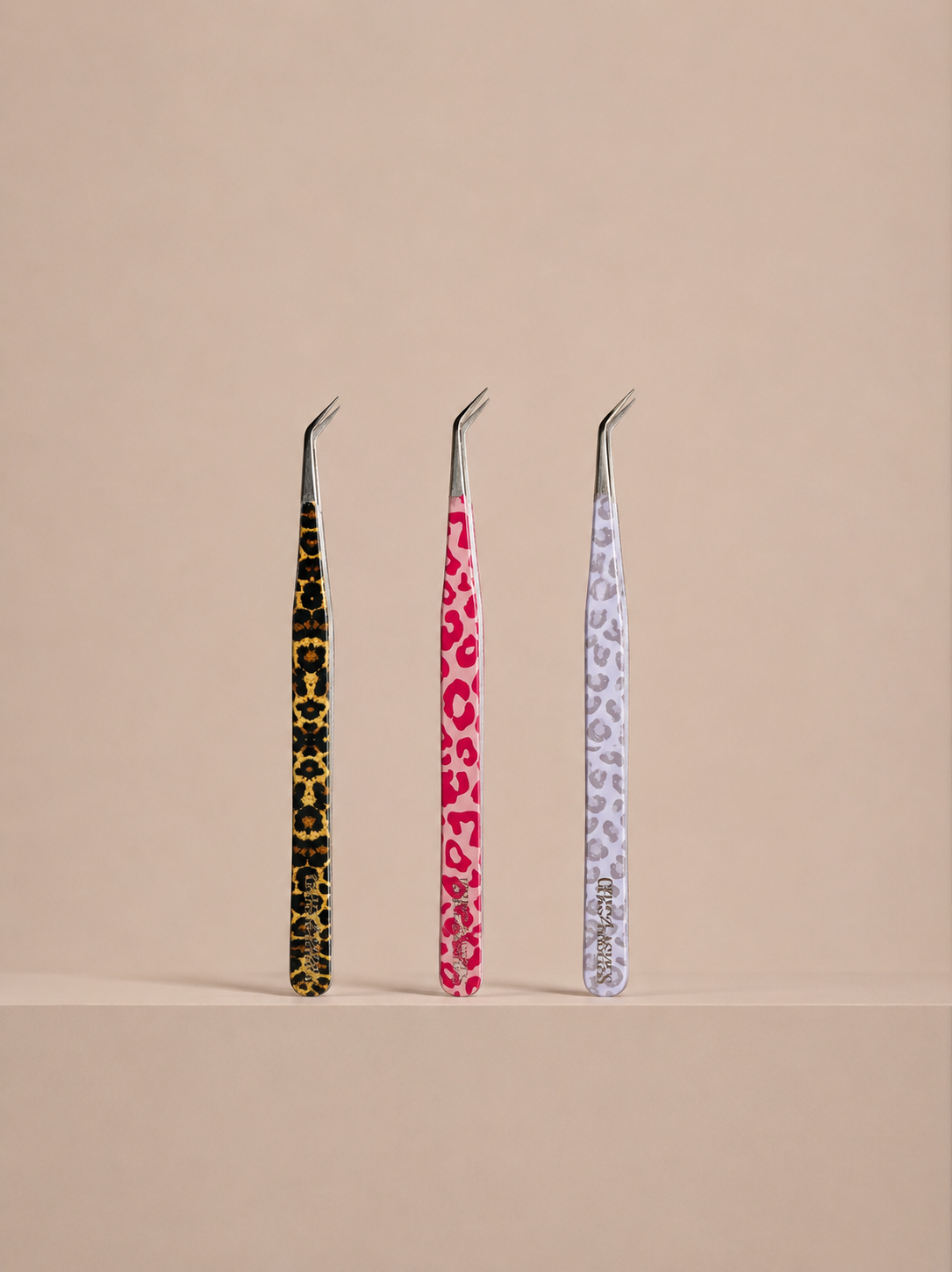 Three pairs of tweezers with patterned handles on a beige background