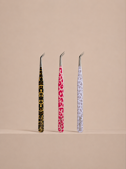 Three pairs of tweezers with patterned handles on a beige background