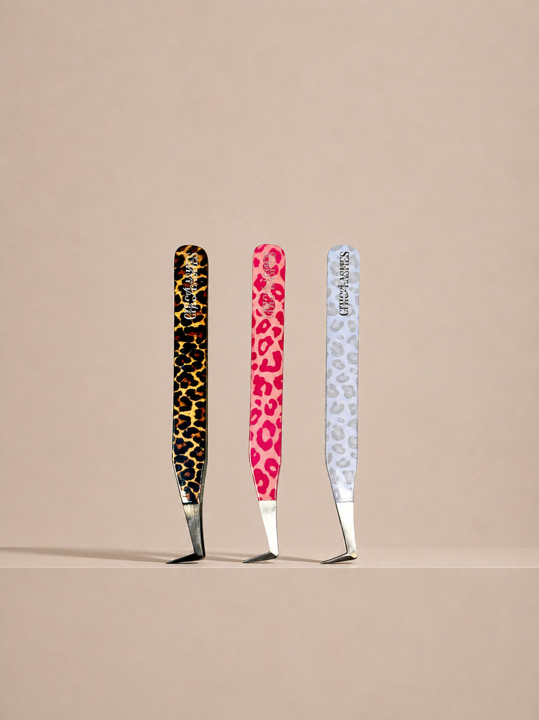 Three pairs of tweezers with colorful handles on a beige background